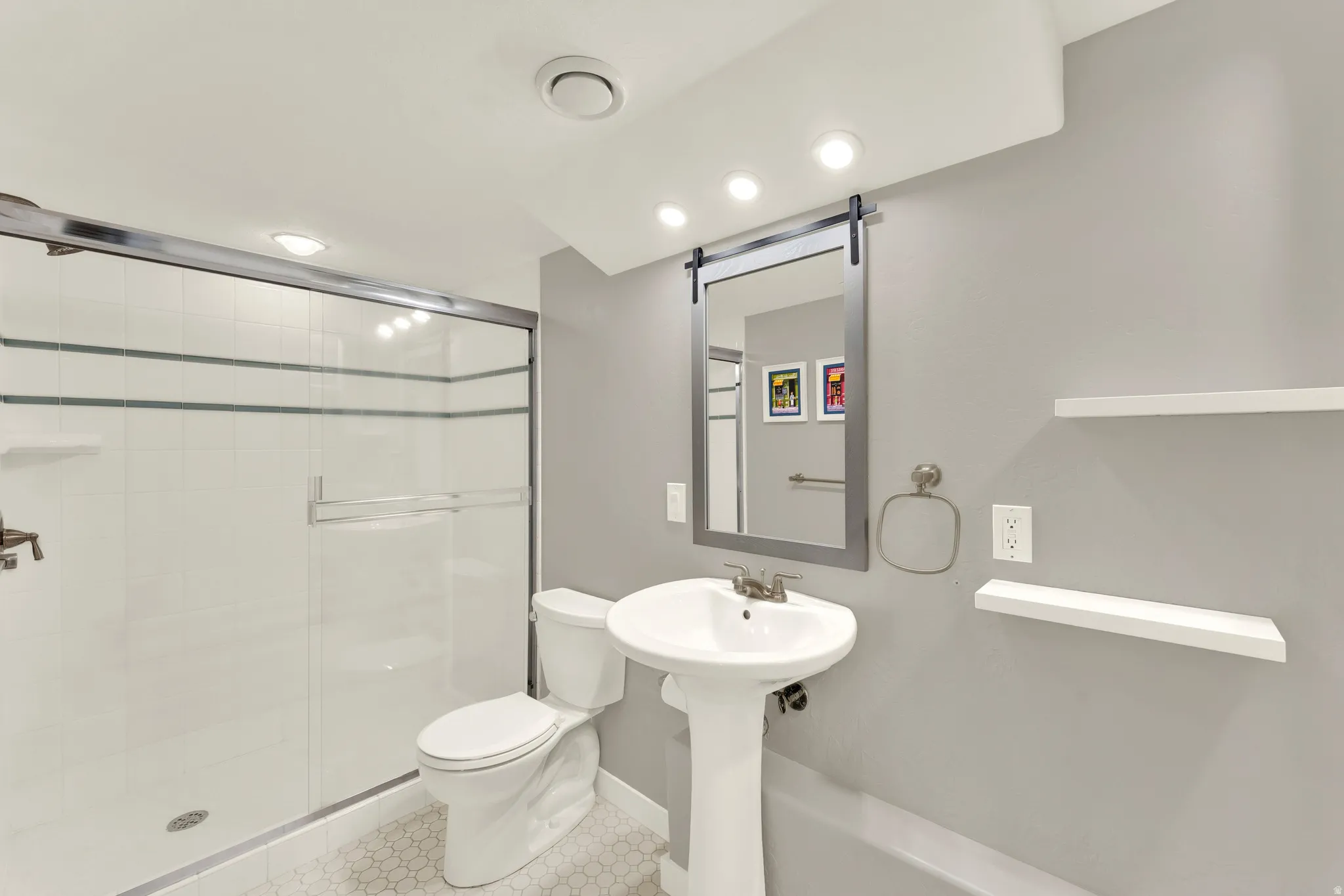 Shower with sliding glass doors, pedestal sink, wall-mounted mirror with integrated lighting, and two floating wall shelves