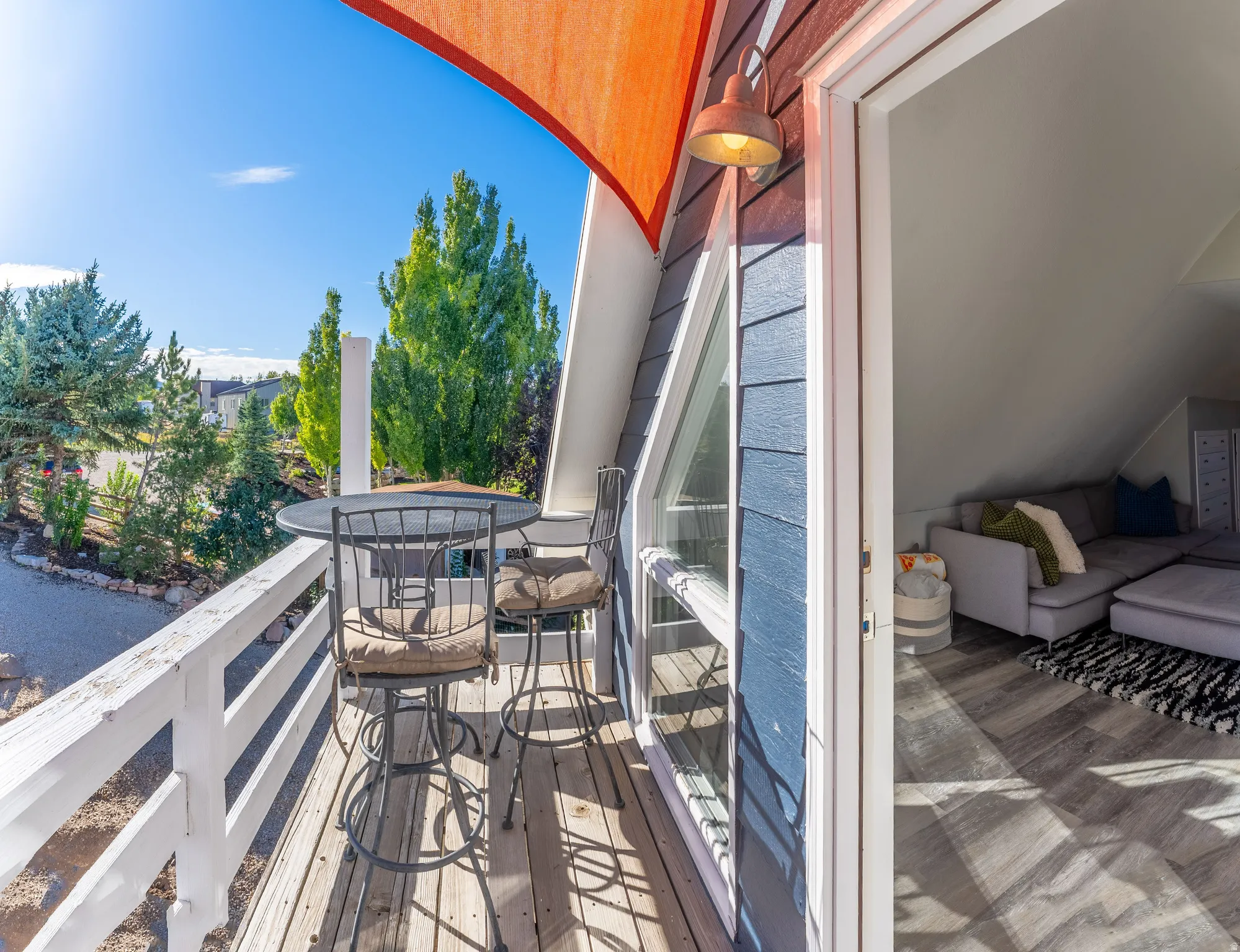 Outdoor balcony with wood decking, white railing, and an orange shade sail