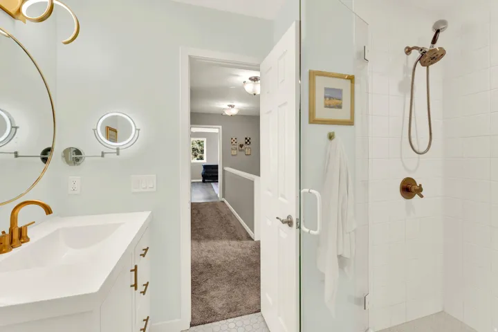 Bathroom featuring a white vanity, integrated sink, gold-finish faucet, and a large round mirror
