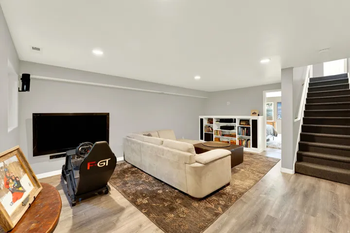 Recessed lighting illuminates the open-concept living space, featuring wood-finish flooring and a built-in shelving unit