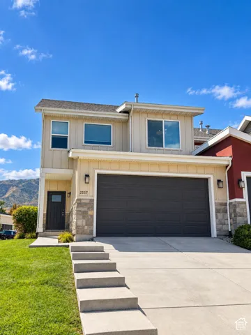 Two-story facade with light-colored siding, dark gray garage door, stone accent details, and prominent front door