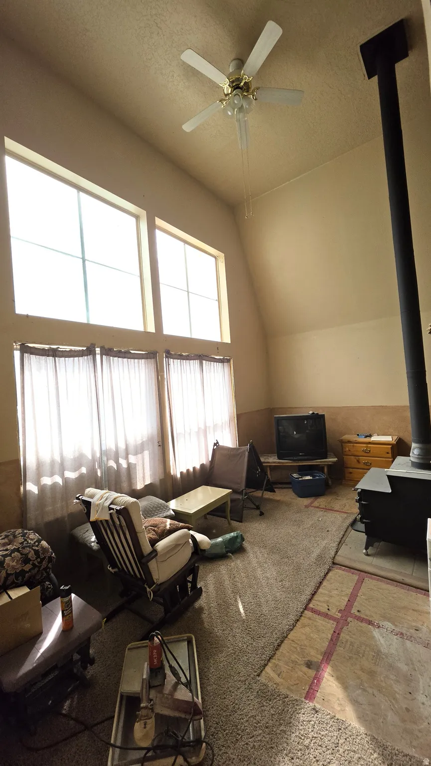 Vaulted ceiling with a ceiling fan, dual upper-story windows, and a wood-burning stove
