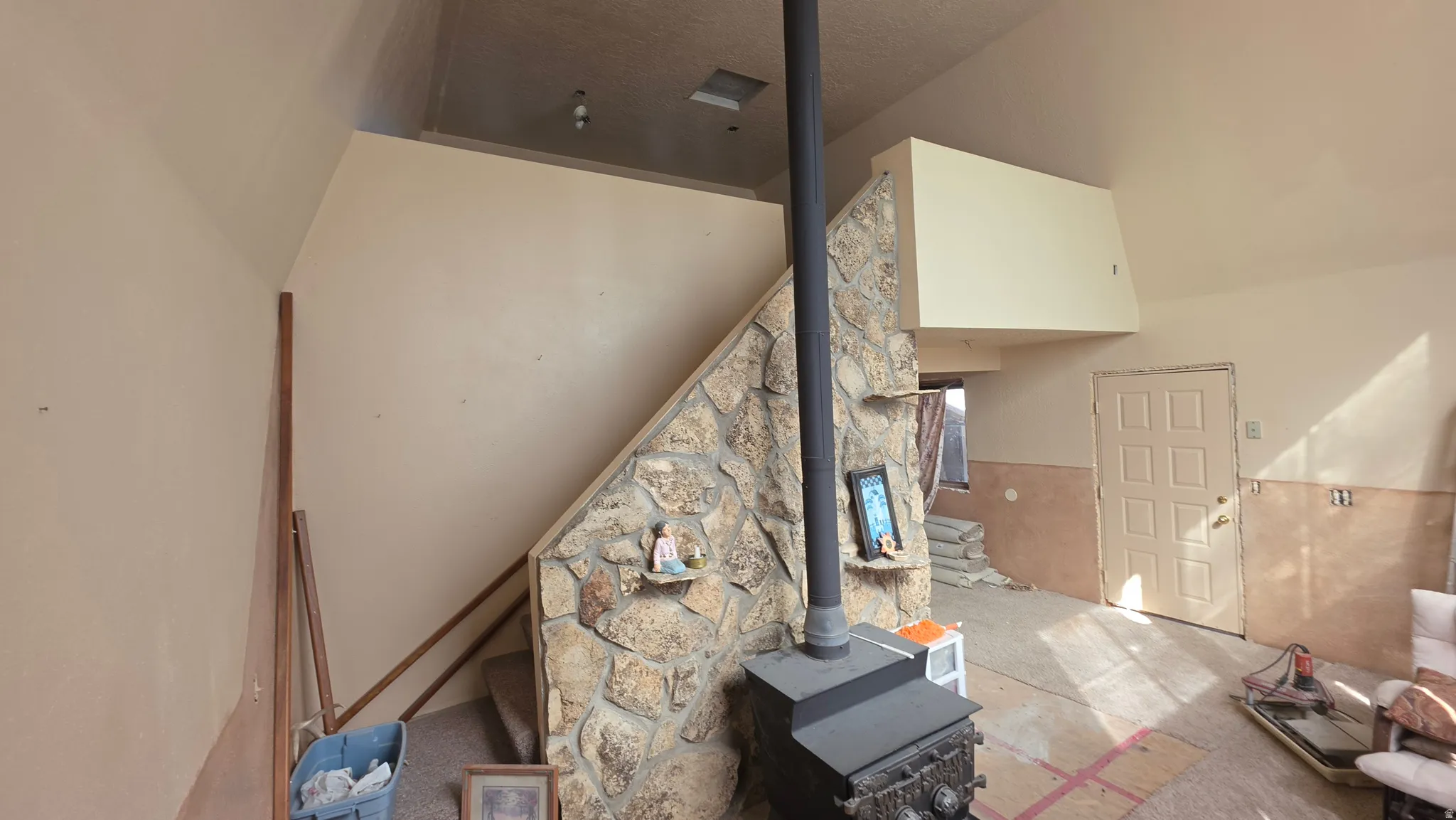 Vaulted ceilings, stone accent wall, wood-burning stove, built-in shelving, and paneled door
