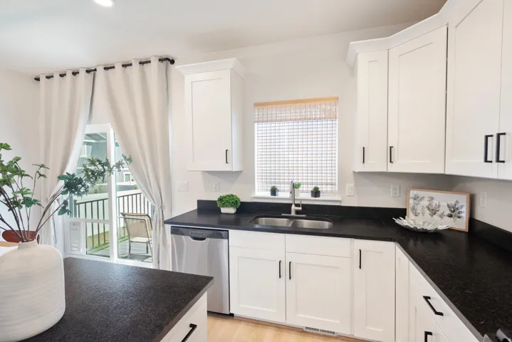 White shaker cabinetry, dark countertops, stainless steel dishwasher, and a double basin sink