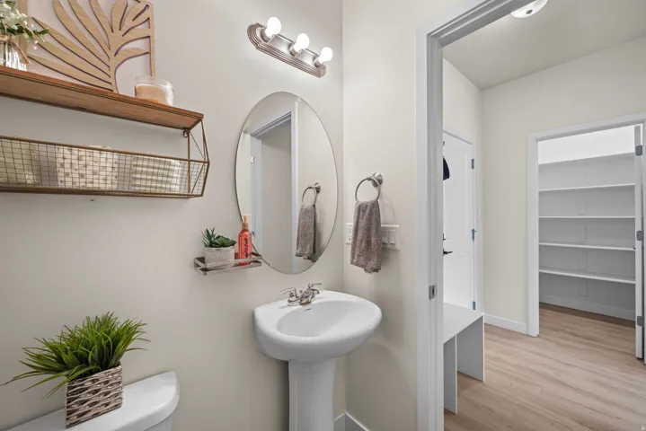 Pedestal sink with chrome faucet, oval wall-mounted mirror, and overhead vanity lighting