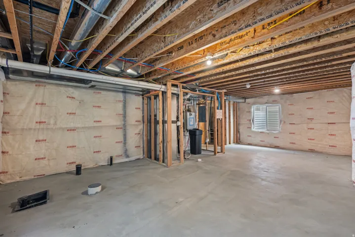 Unfinished basement featuring exposed wood joists, concrete flooring, and an egress window