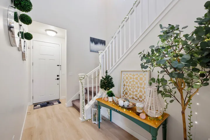 Light wood-finish flooring extending into the entry, white paneled entry door, and white painted staircase with matching balusters