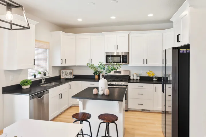 White shaker cabinetry, dark countertops, stainless steel appliances, central island with seating, and light wood-finish flooring