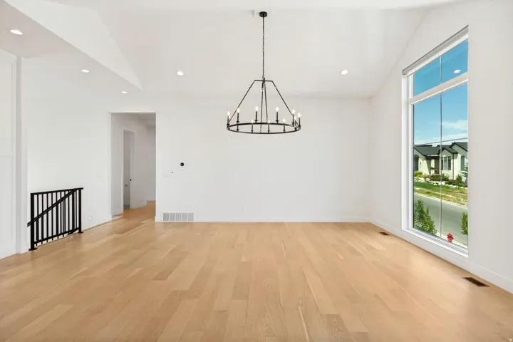 Wood-finish flooring, vaulted ceiling, large accent window, recessed lighting, and a contemporary black chandelier