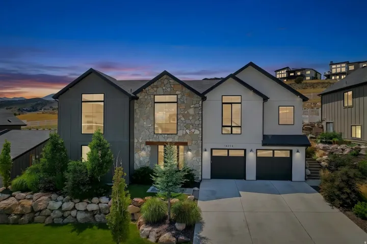 Contemporary exterior featuring stone accents, a dual garage, and expansive windows