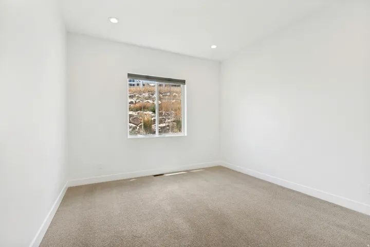 Neutral white walls, recessed ceiling lighting, light-toned carpet, and a window with natural light