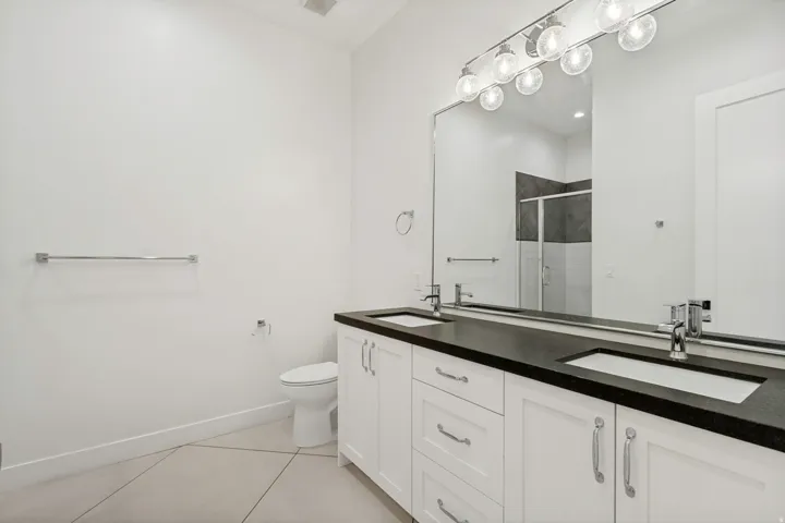 Dual vanity with dark countertop, integrated sinks, chrome fixtures, and white cabinetry