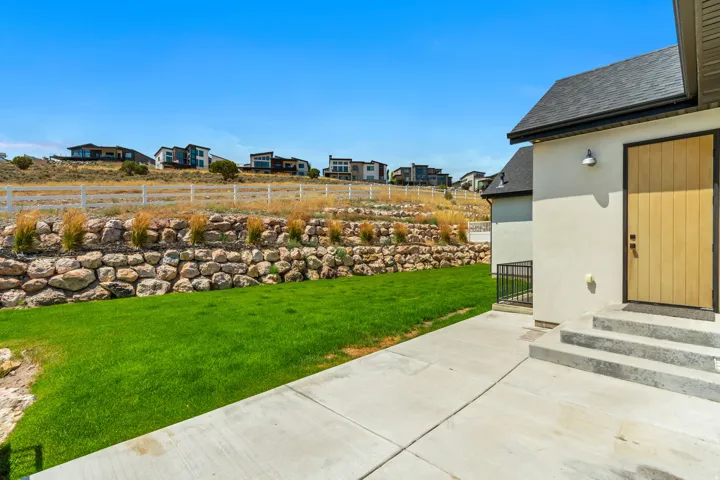 Manicured lawn with a stone retaining wall, concrete patio, and exterior steps