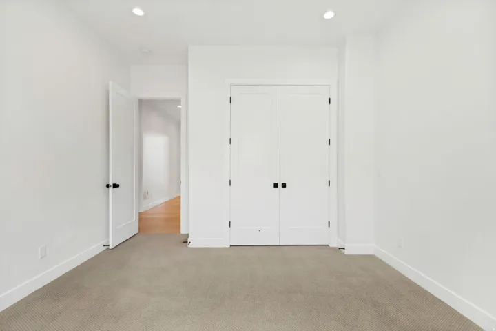 Recessed lighting, white walls, light-colored carpeting, white interior door, and white bi-fold closet doors
