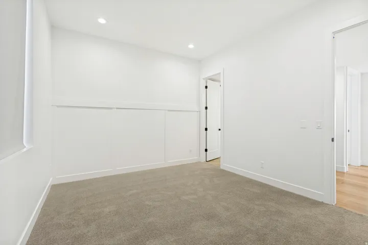 Recessed ceiling lighting, white interior walls, built-in wall paneling, and neutral carpet flooring