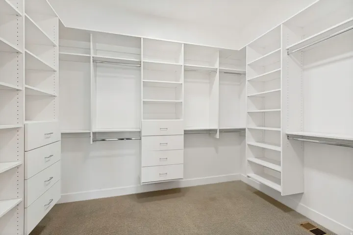 Built-in closet system featuring multiple shelving units, integrated drawers with brushed nickel pulls, and chrome hanging rods