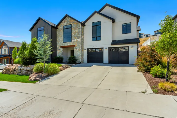 Contemporary exterior with stone and stucco accents, multiple large windows, a two-car garage, and established landscaping