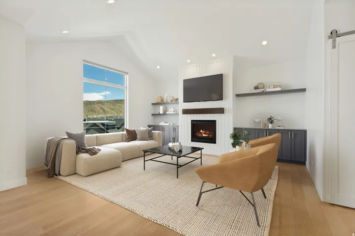 Vaulted ceilings with recessed lighting, wood-finish flooring, a contemporary fireplace with a wood mantel, built-in cabinetry with shelving, and a large picture window