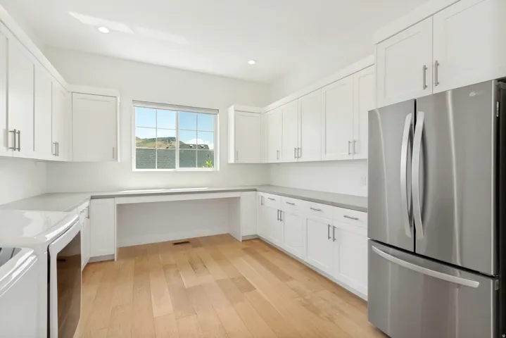Contemporary kitchen featuring white cabinetry, light wood-finish flooring, a built-in desk area, recessed lighting, and a stainless steel refrigerator