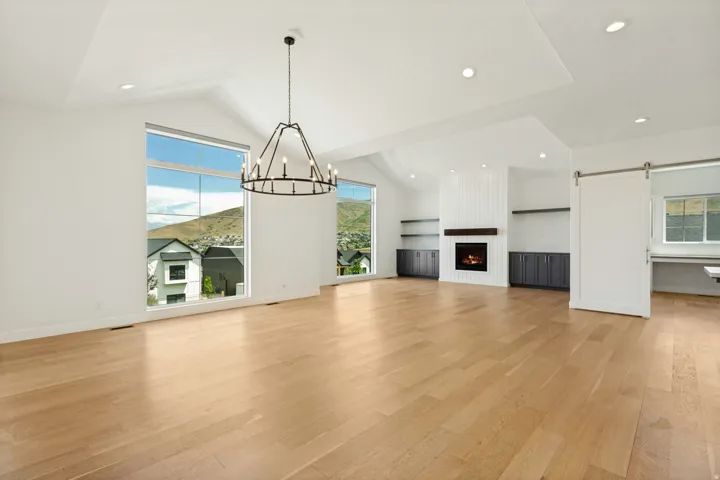 Vaulted ceiling with a contemporary chandelier, recessed lighting, expansive windows, wood-finish flooring, and a fireplace with a wood mantle