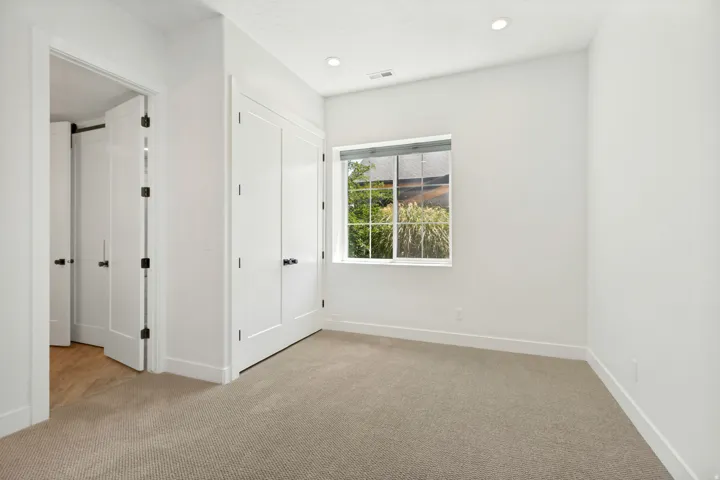 Neutral carpeting, recessed lighting, white walls, and a large window