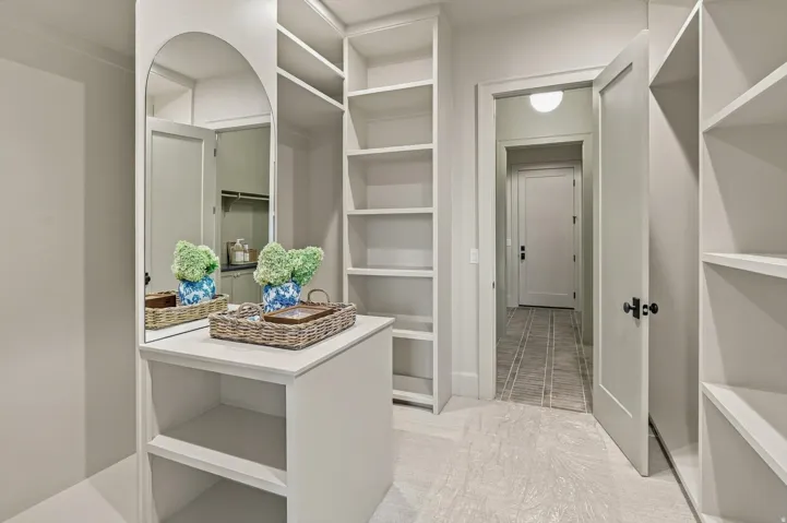 Built-in shelving, arched full-length mirror, light-toned flooring, and a solid core interior door with dark hardware