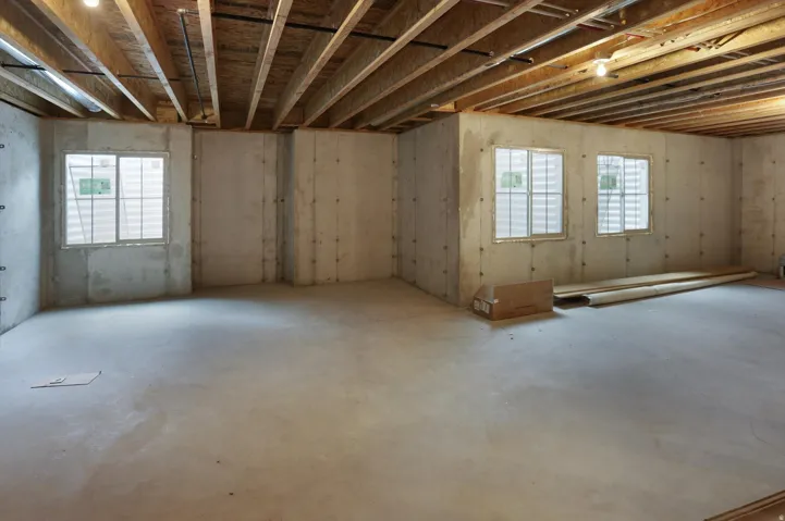 Unfinished concrete flooring, exposed ceiling joists, concrete walls, and multiple windows