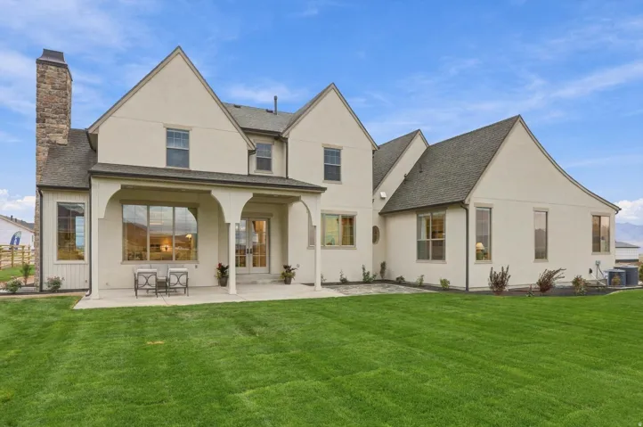 Stucco exterior with a stone chimney and dark shingle roof