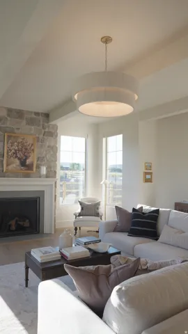 Vaulted ceiling with a drum pendant light, stone fireplace with a white mantel, and wood-finish flooring