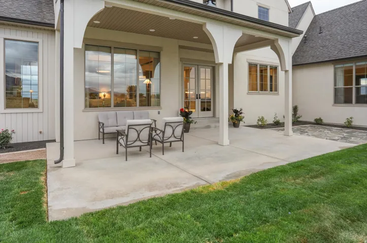 Covered patio with arched supports, concrete hardscaping, large windows, French doors, and natural grass