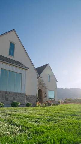 Manicured lawn, stone and stucco exterior, arched entryway, gabled rooflines, and large windows