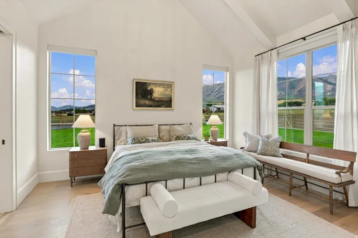 Vaulted ceiling with exposed beams, light wood-finish flooring, large grid-pane windows, and a built-in window bench