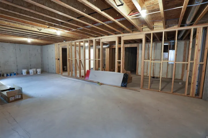 Unfinished lower level featuring concrete flooring, exposed wooden joists, and framed partition walls