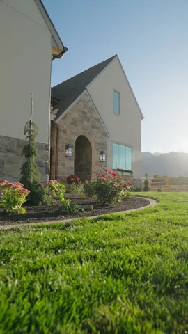 Stone and stucco exterior, arched entry, exterior wall sconces, large pane window, and landscaped front yard