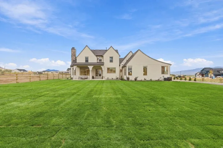 Expansive green lawn bordering a stucco exterior with a covered patio, gabled rooflines, and a visible chimney feature