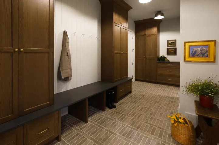Brick-patterned flooring, built-in wooden cabinetry, integrated bench seating, and wall-mounted coat hooks