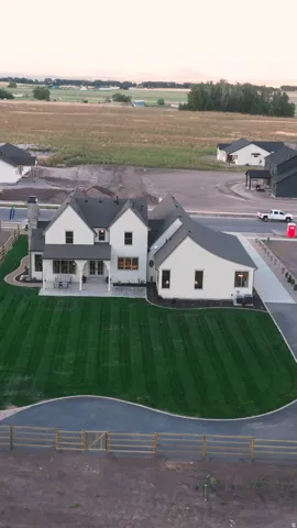 White exterior with dark roof, expansive green lawn, curved paved driveway, paved patio, and a stone chimney