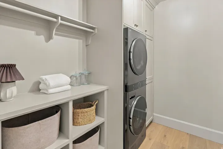 Built-in shelving, stacked laundry appliances, upper cabinetry, wood-finish flooring, and a hanging rod