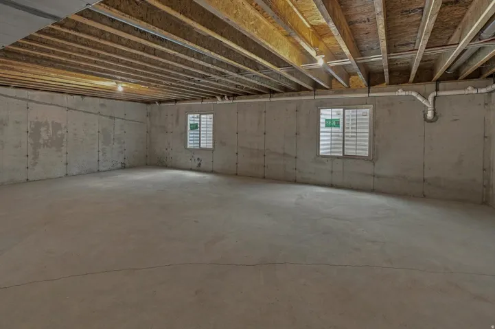 Concrete flooring and walls with exposed ceiling joists and two windows