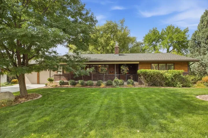 Expansive lawn, mature tree, well-maintained landscaping, covered front porch, and brick chimney