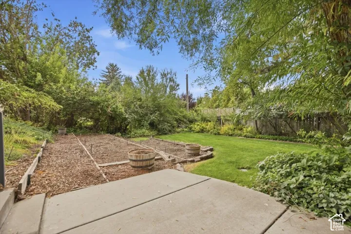 Expansive backyard featuring a concrete patio, landscaped garden beds, lush lawn, and mature trees
