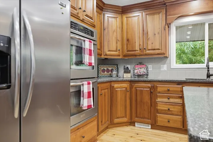 Stainless steel double wall ovens, wood-finish cabinetry, granite countertops, light wood-finish flooring, and a tiled backsplash