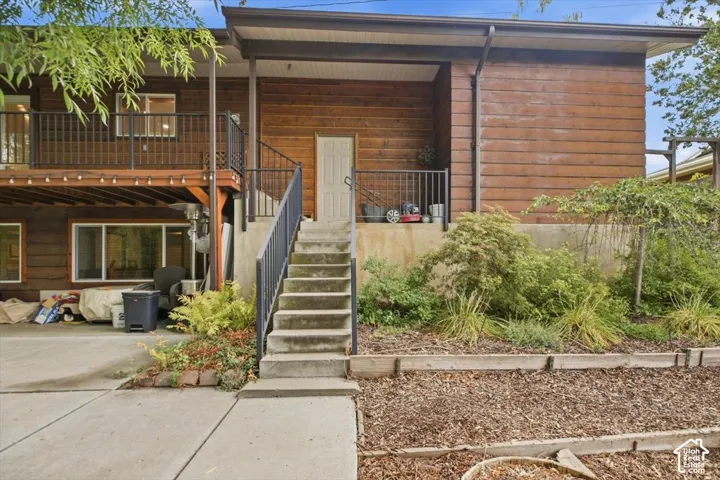 Wood-paneled exterior featuring a covered porch with a black railing, an upper-level balcony, concrete stairs, and a landscaped garden bed