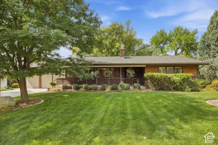 Expansive lawn, mature tree, well-maintained landscaping, covered front porch, and brick chimney