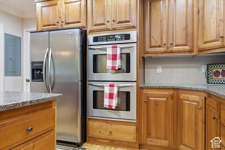 Stainless steel refrigerator, double ovens, extensive wood cabinetry, granite-style countertops, and a subway tile backsplash