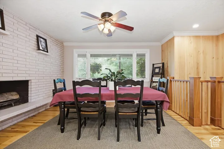 Dining space featuring wood-finish flooring, a white brick fireplace, wood paneling, and a window with blinds