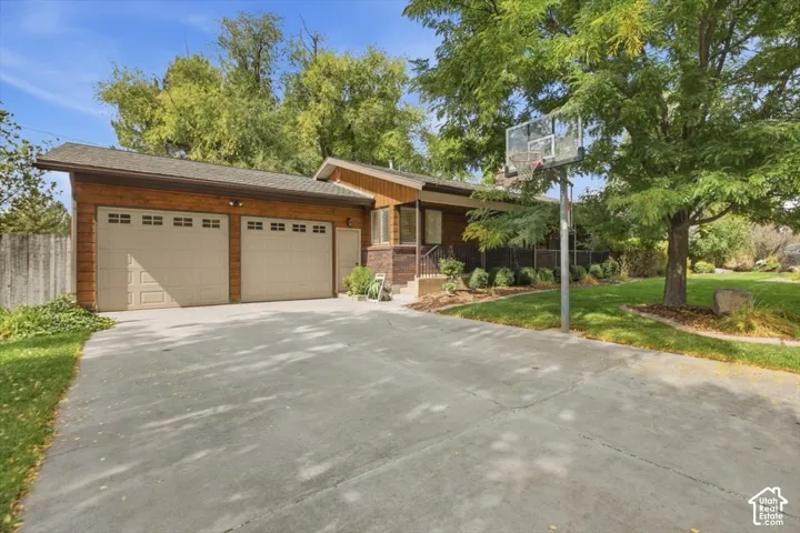 Expansive concrete driveway, two-car garage with panel doors, natural wood siding, mature landscaping, and established trees