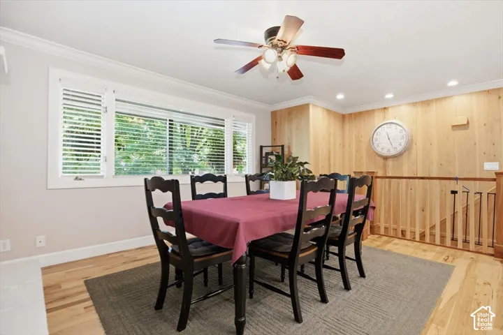 Wood-finish flooring, accent wood paneling, crown molding, multiple windows with plantation shutters, and a ceiling fan with integrated lighting