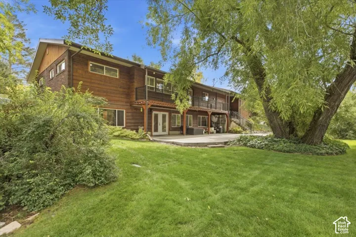 Expansive green lawn with a large mature tree, concrete patio, and a two-story wood-sided exterior featuring multiple windows and a second-story balcony