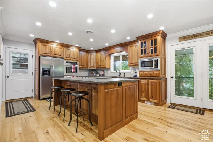 Kitchen featuring wood-finish flooring, wood cabinetry, recessed lighting, a central island with a stone countertop, and stainless steel appliances
